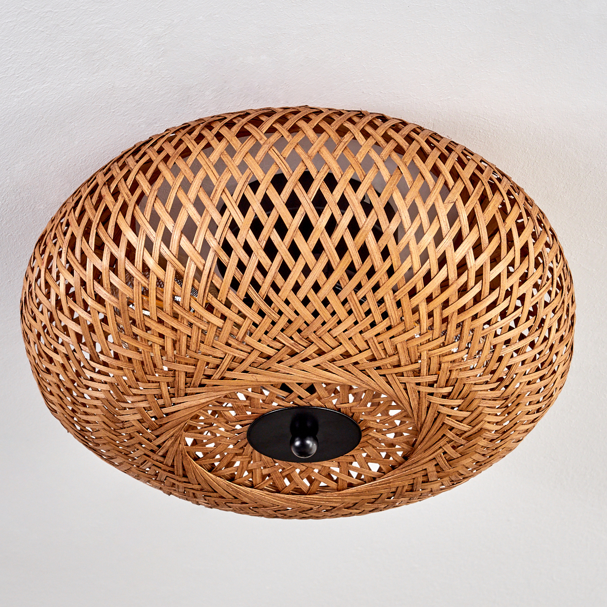 Geflochtene Deckenlampe mit schwarzer zentraler Halterung. Die Lampe ist aus braunem Rattan gewebt, mit weißem Deckenhintergrund.