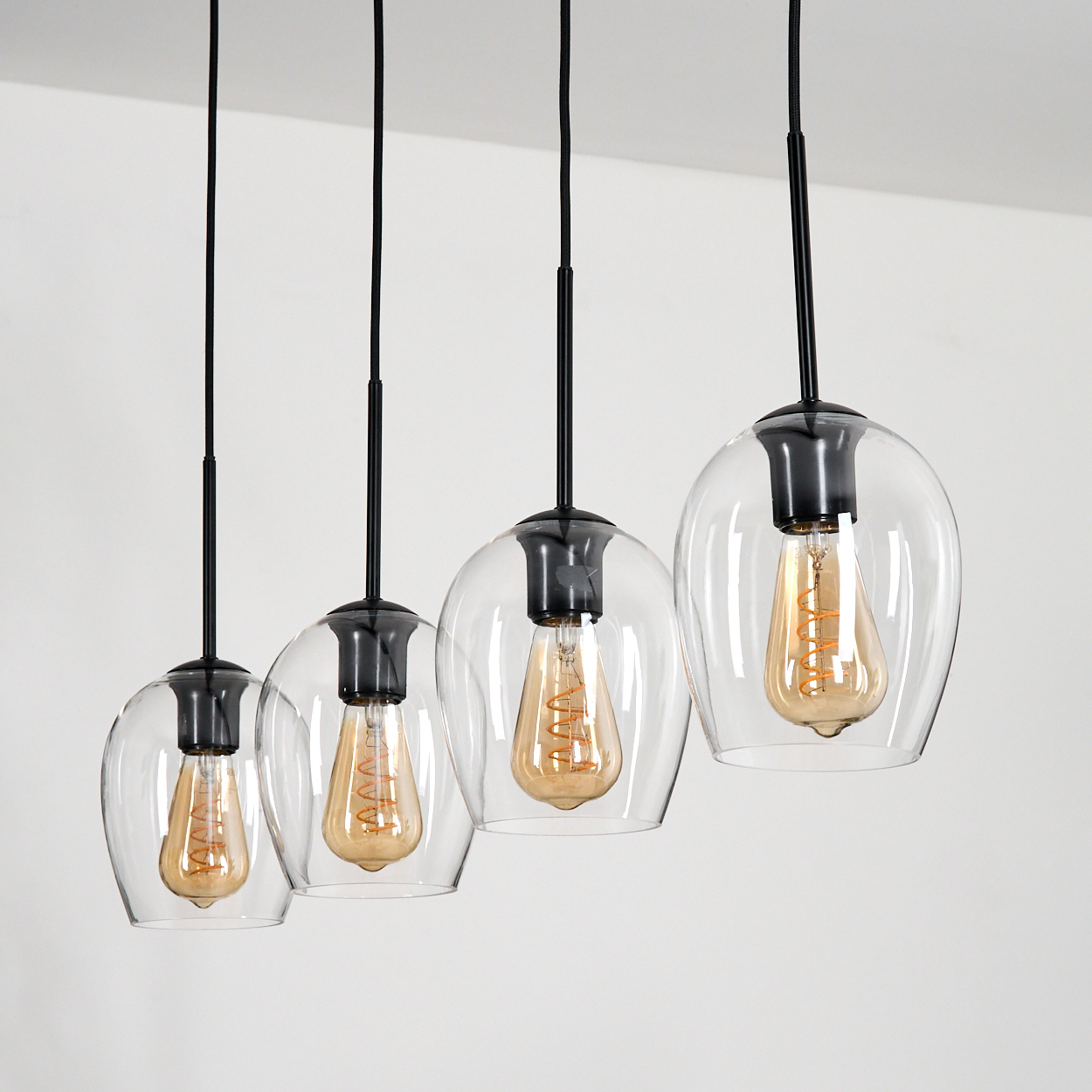 Vier Pendelleuchten mit klaren Glasschirmen und Edison-Glühbirnen hängen vor weißem Hintergrund.