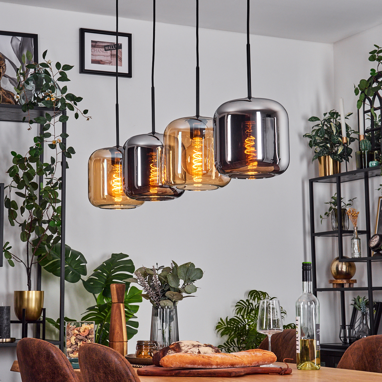 Esszimmer mit Hängelampen. Tisch mit Brot, Wein und Gläsern gedeckt. Grüne Pflanzen in Regalen und Töpfen.