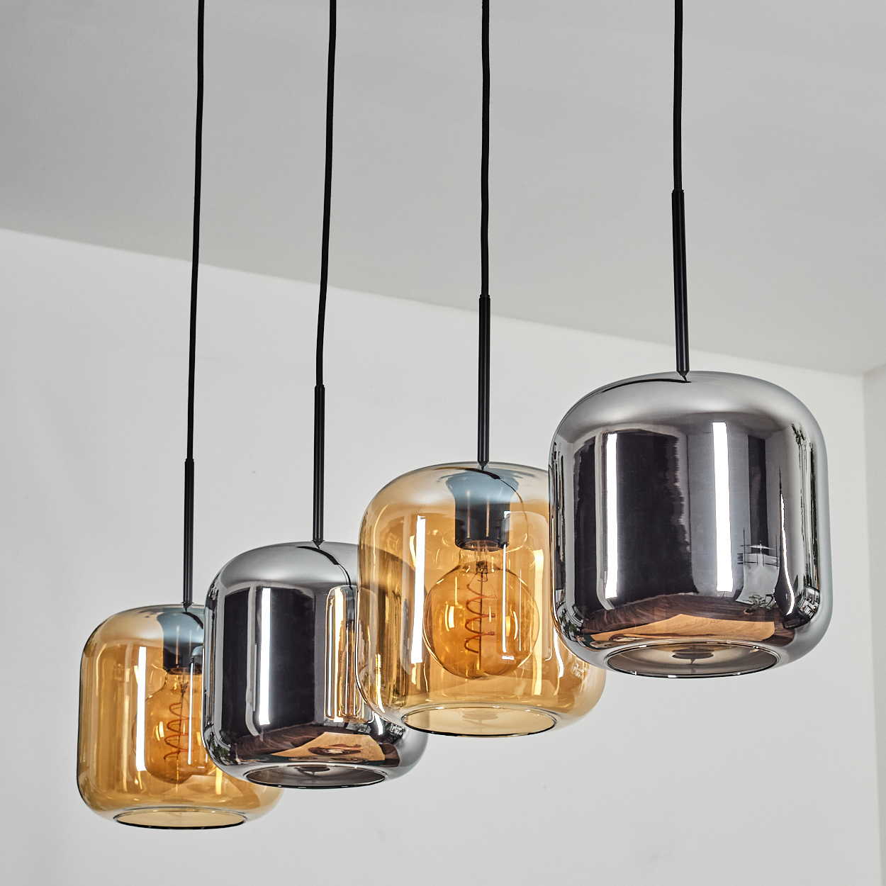 Vier Pendelleuchten mit Glas- und Chromschirmen hängen von einer weißen Decke. Jede hat eine sichtbare Glühbirne.