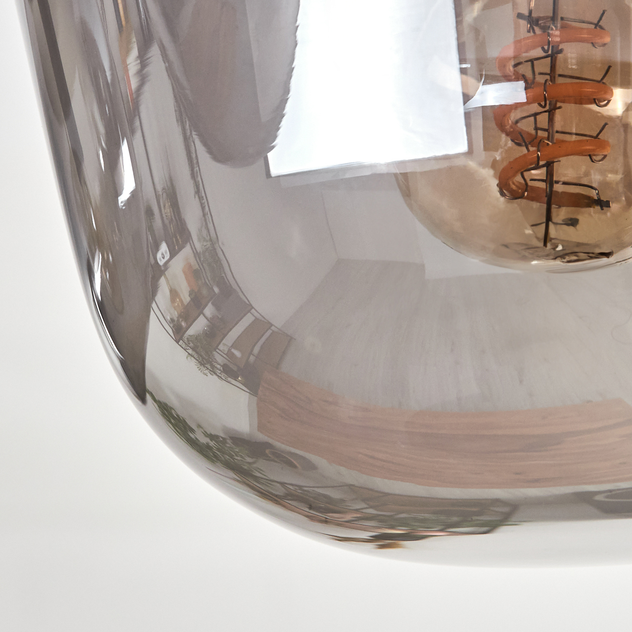 Nahaufnahme einer Glühbirne mit klarem Glasschirm. Die Glühbirne hat einen braunen Glühfaden und der Schirm reflektiert die Umgebung.
