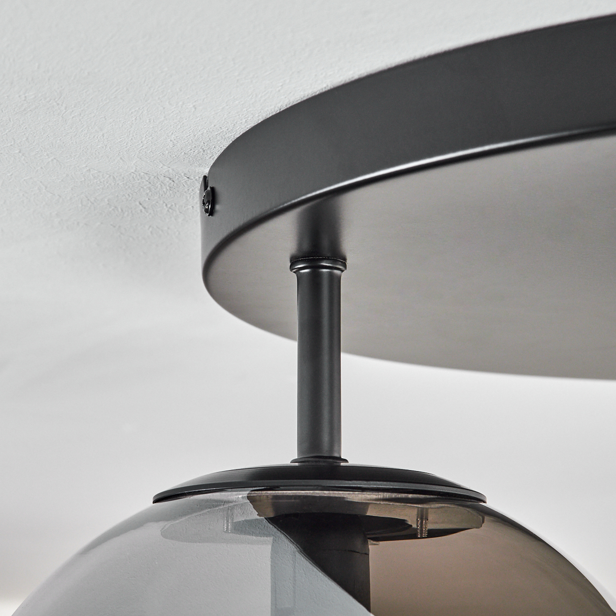 Nahaufnahme einer Deckenlampe. Sie hat einen dunklen Metallsockel und einen Rauchglasschirm, der an einer weißen Decke befestigt ist.