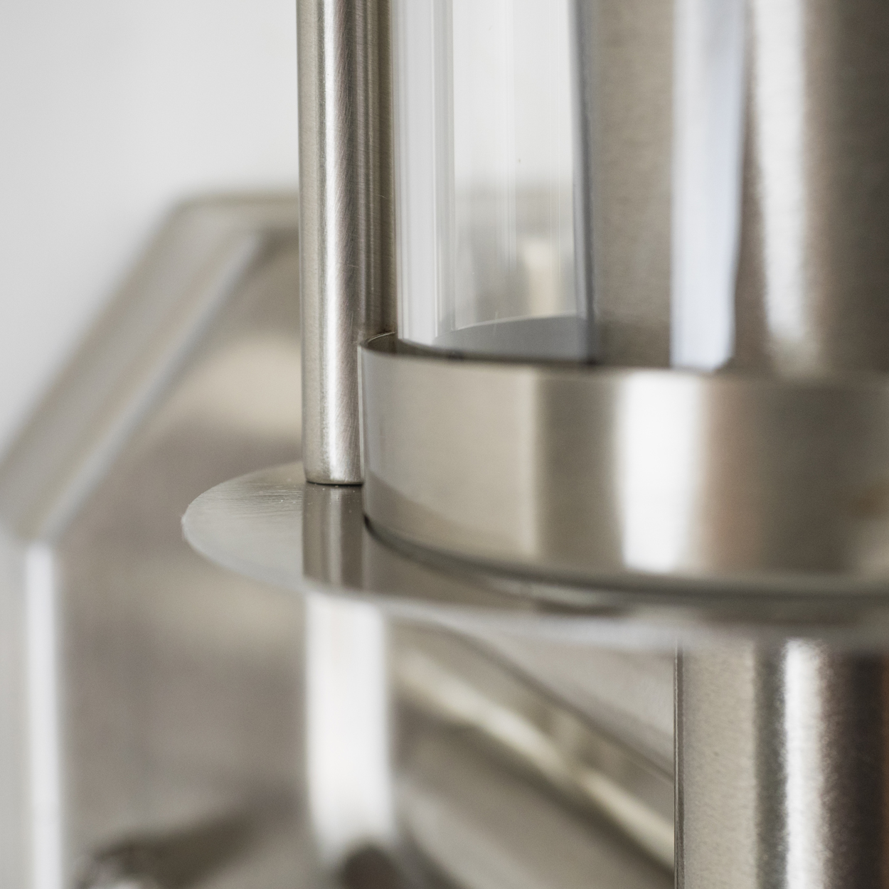 Nahaufnahme einer metallischen Lampe mit einem durchsichtigen Glaszylinder. Die Lampenstruktur ist silberfarben, mit rundem Sockel und vertikalem Rohr.