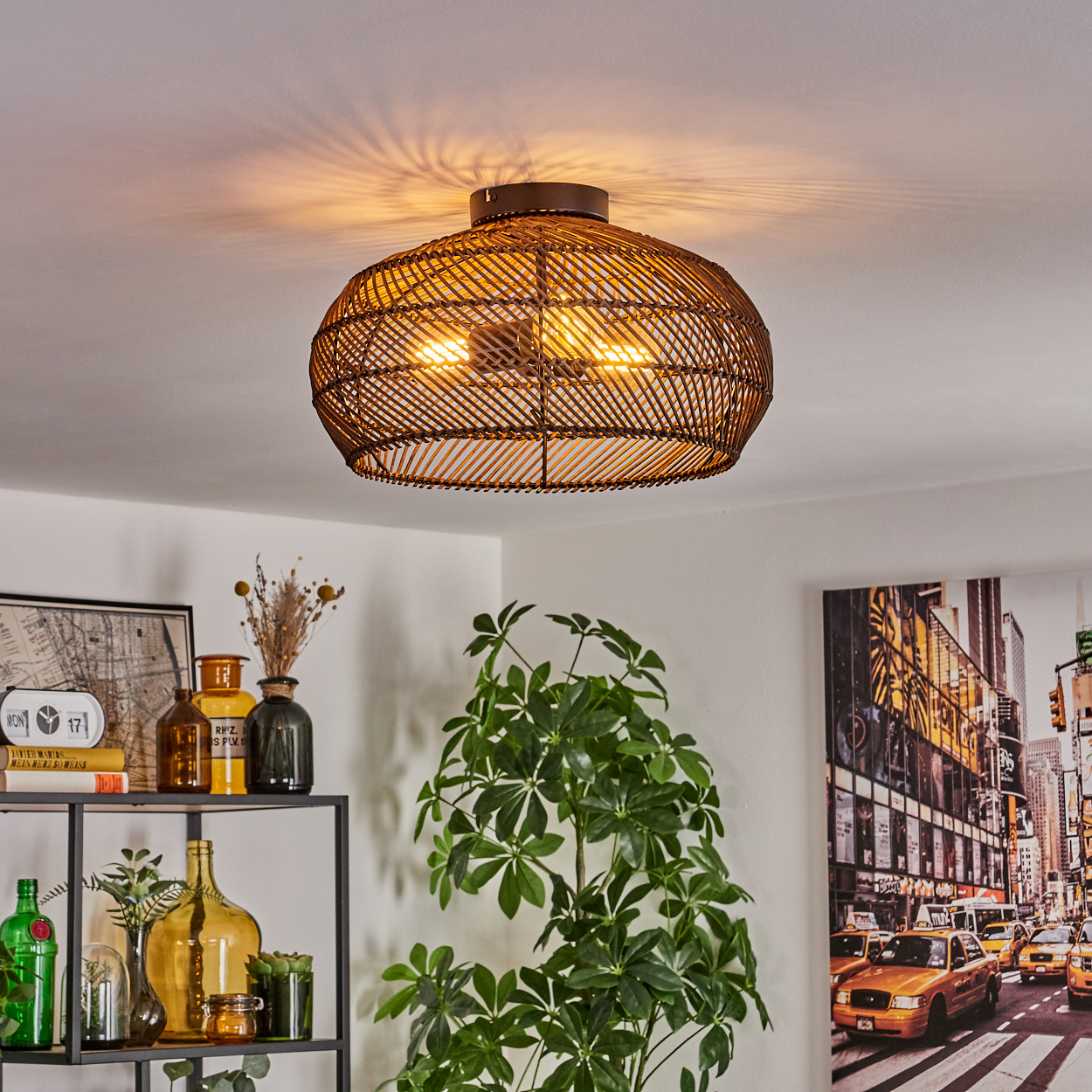 Eine gewebte braune Deckenlampe beleuchtet einen Raum mit einer Pflanze, einem Regal mit Flaschen und einem New York City-Bild.