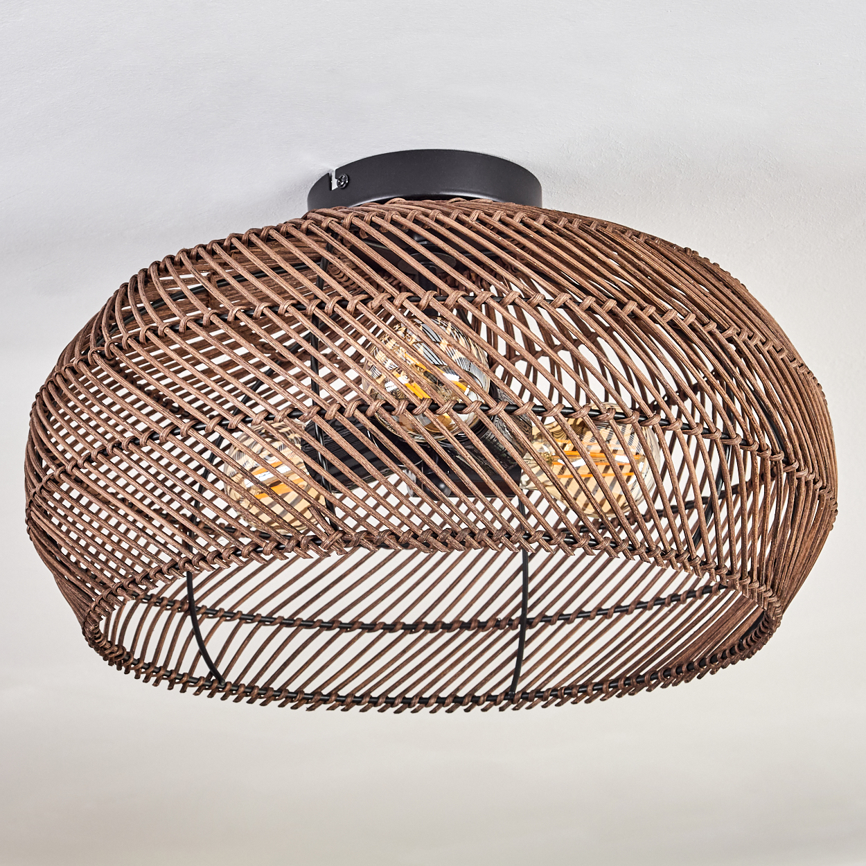 Eine braune Deckenlampe aus gewebtem Rattan mit sichtbaren Glühbirnen, die an einer weißen Decke montiert ist.