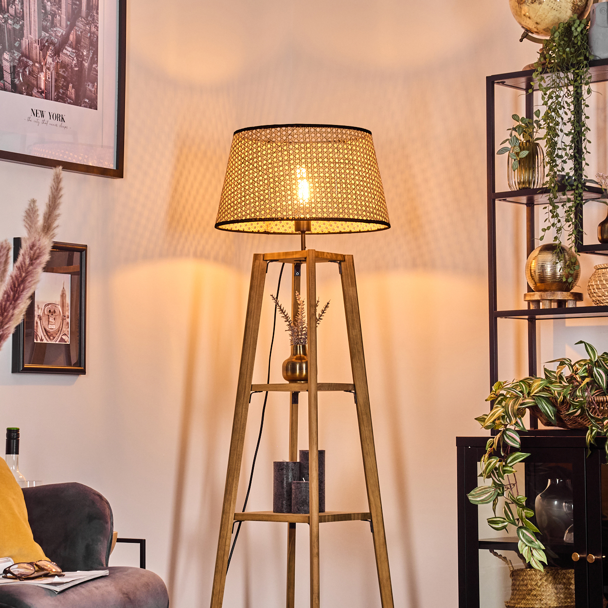 Eine beleuchtete Stehlampe aus Holz mit einem gewebten Schirm steht in einem Raum. Dahinter stehen Regale.