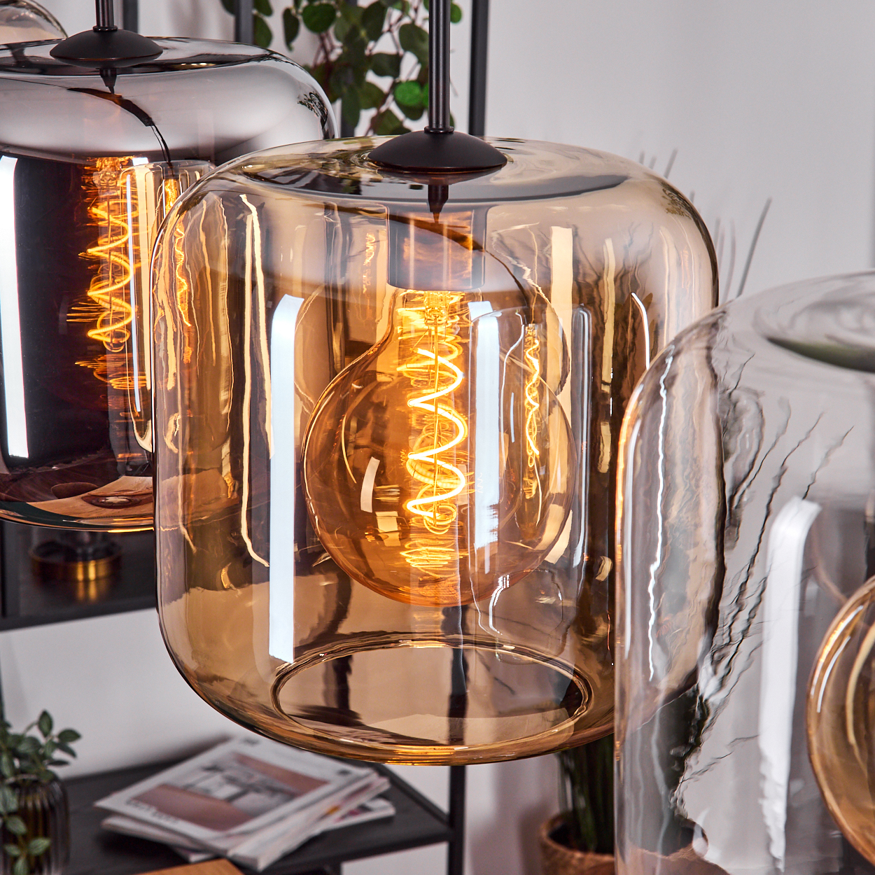Nahaufnahme von drei Glas-Pendelleuchten mit freiliegenden Glühbirnen mit Spiralfilamenten. Die Glasschirme sind bernsteinfarben und klar.