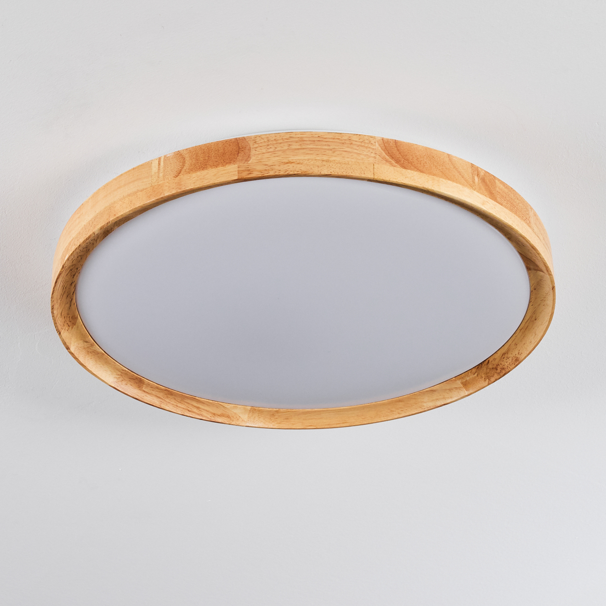Eine holzgerahmte, ovale Deckenleuchte. Die Leuchte hat eine weiße Mitte und einen hellbraunen Holzrahmen, montiert an einer weißen Decke.