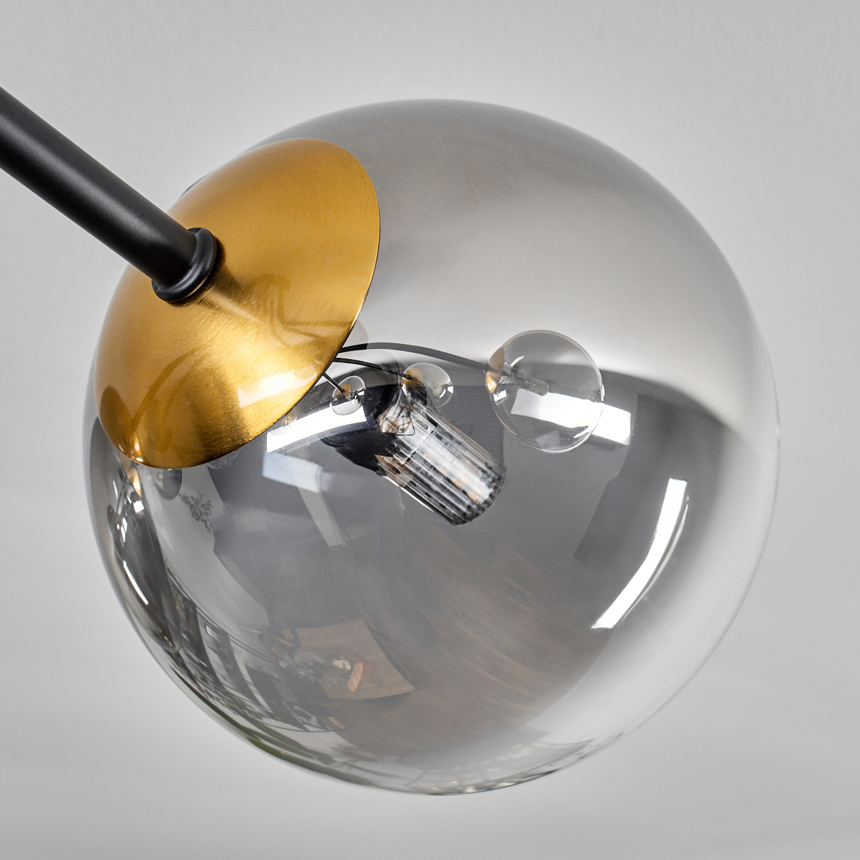 Eine moderne Lampe mit kugelförmigem Glasschirm, goldenem Akzent und schwarzem Arm. Die Lichtquelle ist sichtbar.