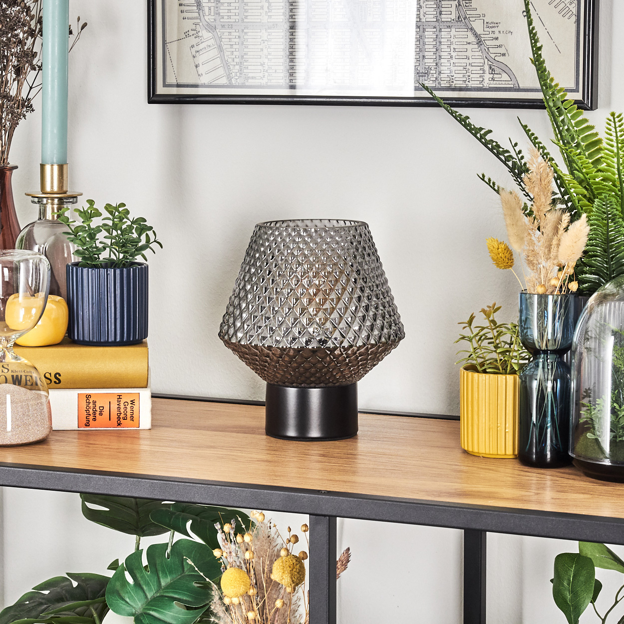 Ein Holzregal mit Lampe, Pflanzen, Büchern und Dekorationsartikeln. Die Lampe hat einen grauen Glasschirm. Grüne Pflanzen und eine Karte im Hintergrund.