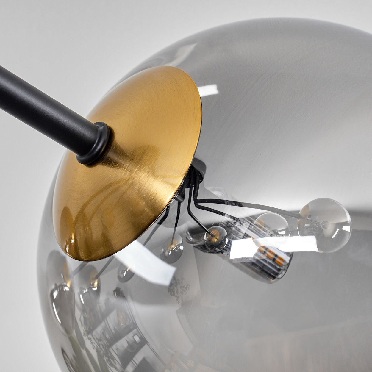 Nahaufnahme einer modernen Lampe. Ein schwarzer Stab trägt eine goldene Scheibe und eine rauchige Glaskugel mit kleinen Glühbirnen.