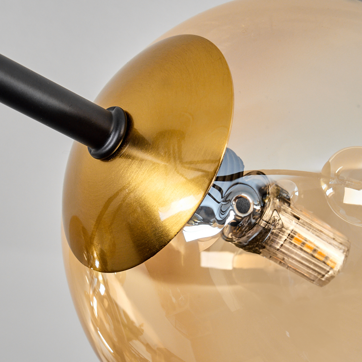 Nahaufnahme einer modernen Lampe. Sie hat einen goldenen Schirm, eine transparente Glaskugel und einen schwarzen Arm mit LED-Glühbirne.