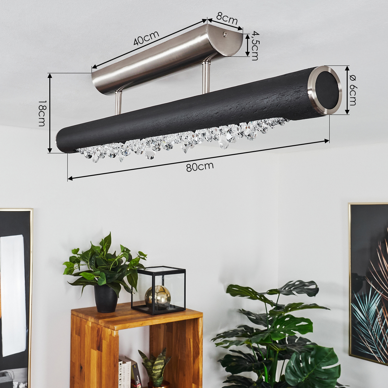 Eine schwarz-silberne Deckenlampe wird gezeigt. Darunter hängen dekorative Kristalle. Pflanzen und ein Holzregal sind im Vordergrund.