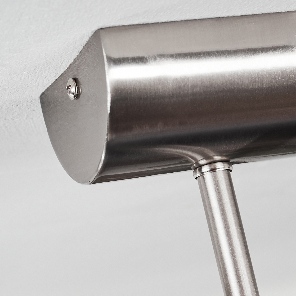 Nahaufnahme einer Lampenhalterung aus gebürstetem Metall an einer weißen Decke. Eine Schraube befestigt die Halterung. Der Arm ragt nach unten.
