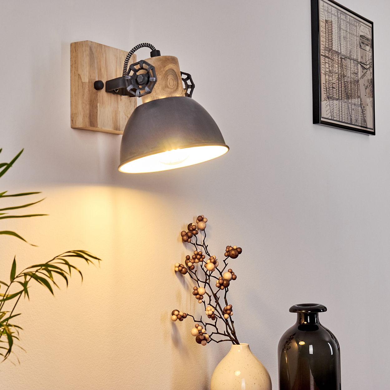 An der weißen Wand ist eine Wandlampe mit Holzsockel und Metallschirm angebracht. Unten sind Vasen mit Pflanzen.