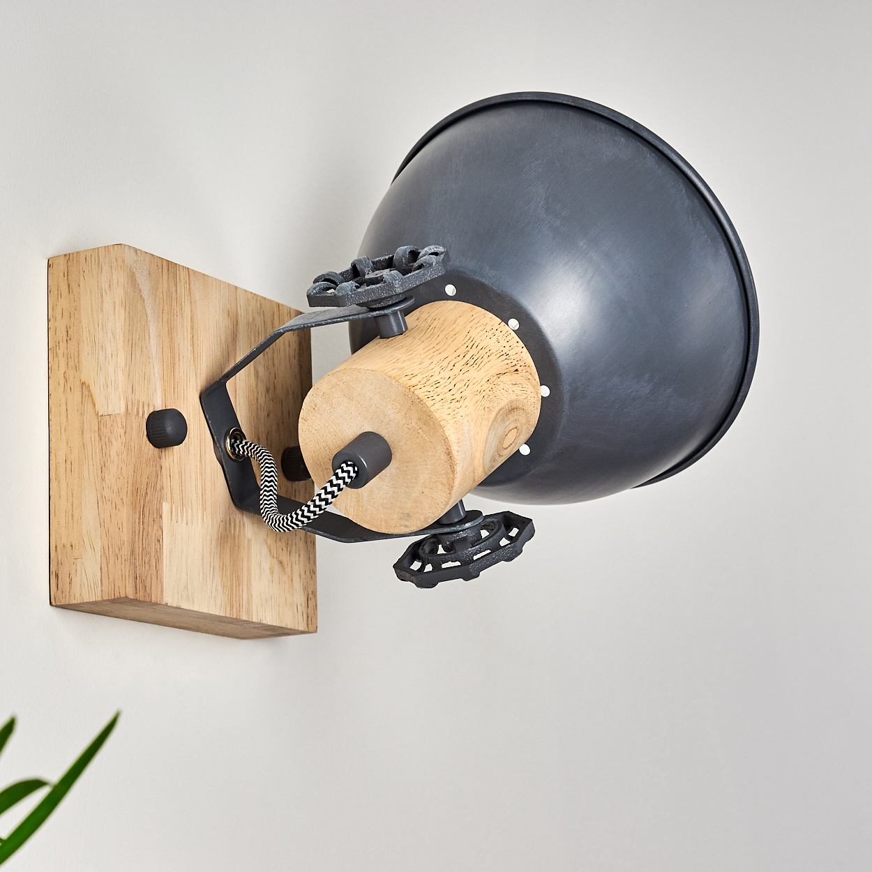 Eine Wandlampe mit Holzsockel und Zylinder, schwarzem Lampenschirm und schwarz-weißem Kabel, montiert an einer weißen Wand.