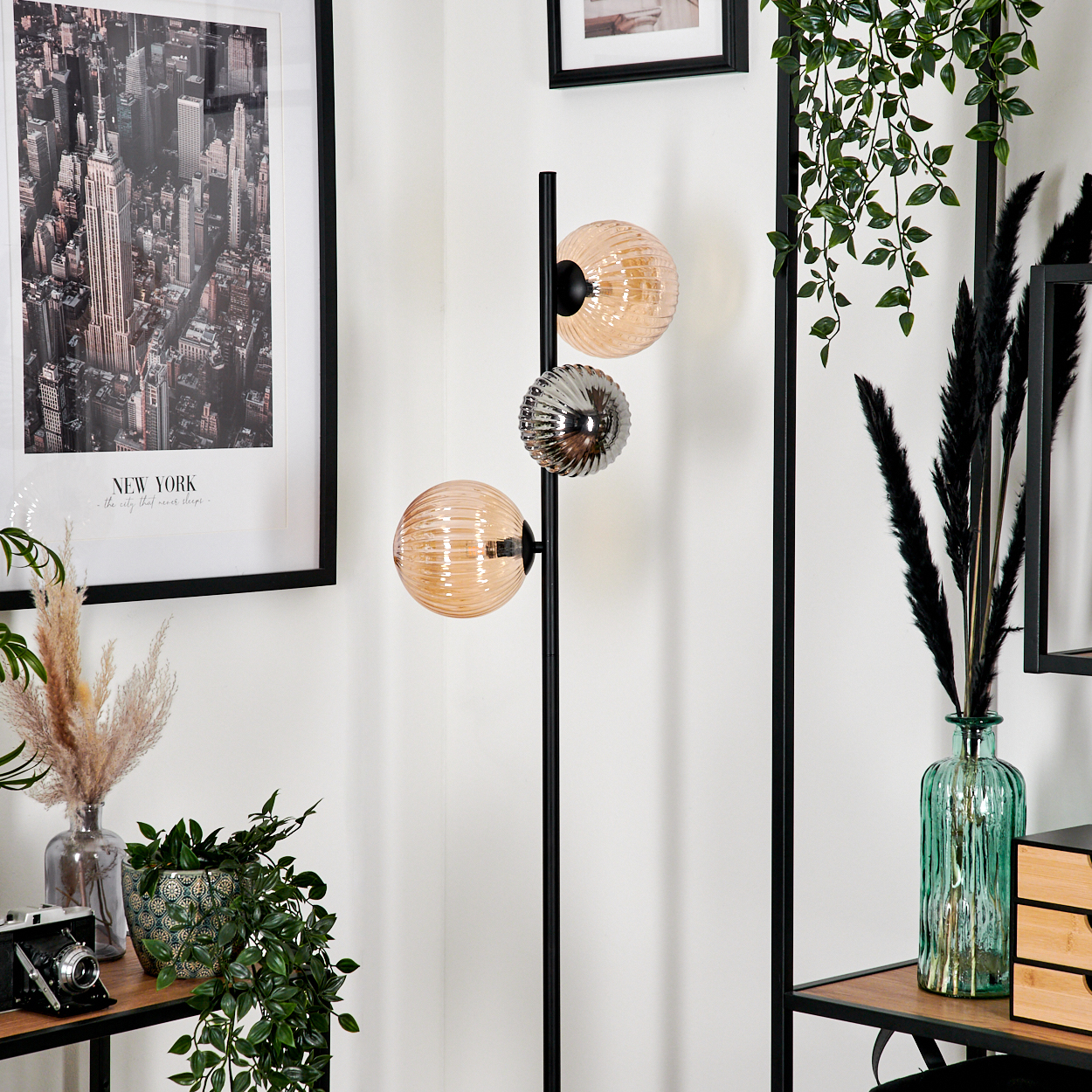 Raumecke mit Lampe, New York Poster, Pflanzen und Kamera auf einem Holztisch. Die Lampe hat drei Glaskugeln.