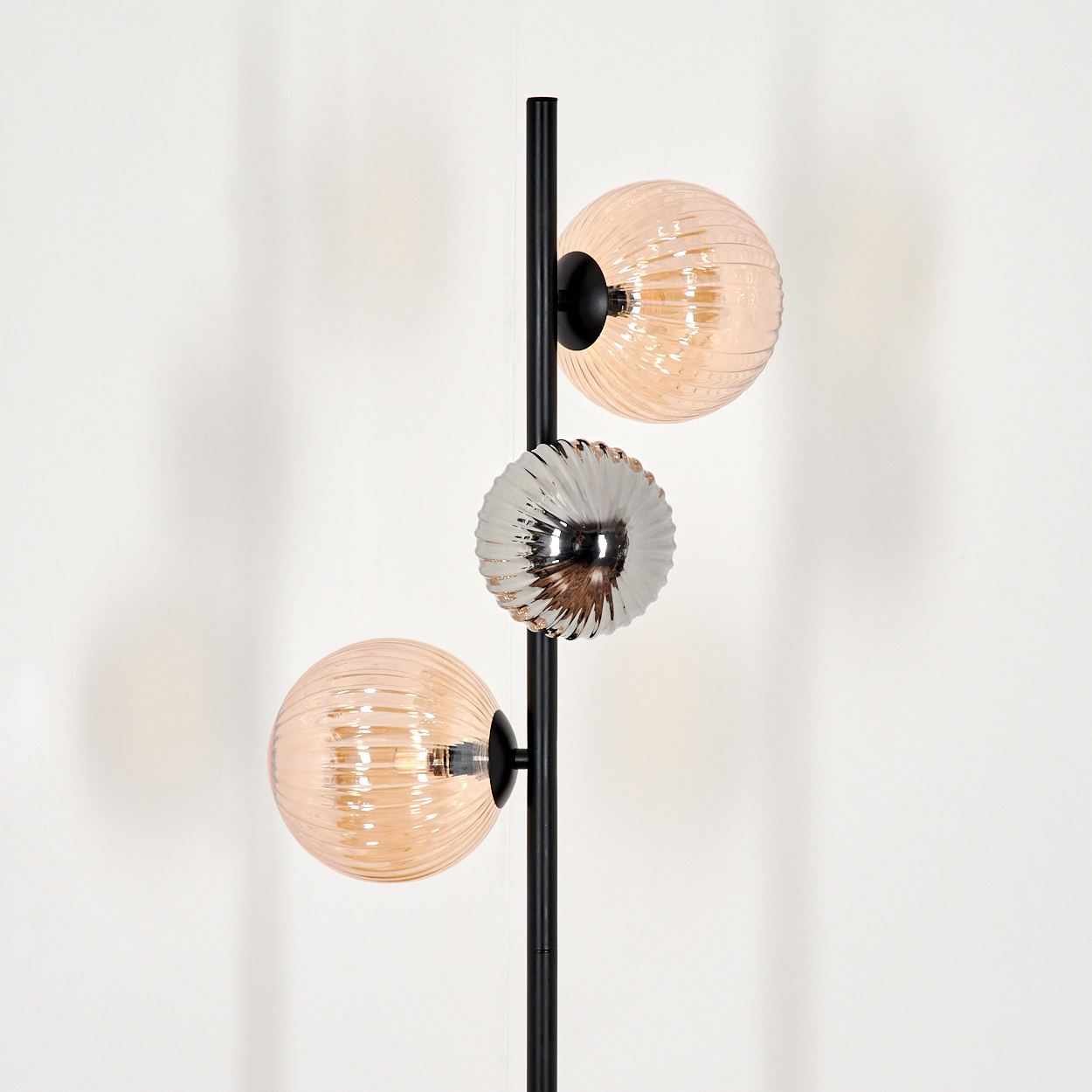 Eine moderne Stehlampe mit schwarzem Mast und drei Glasschirmen. Zwei sind pfirsichfarben, einer silberfarben.