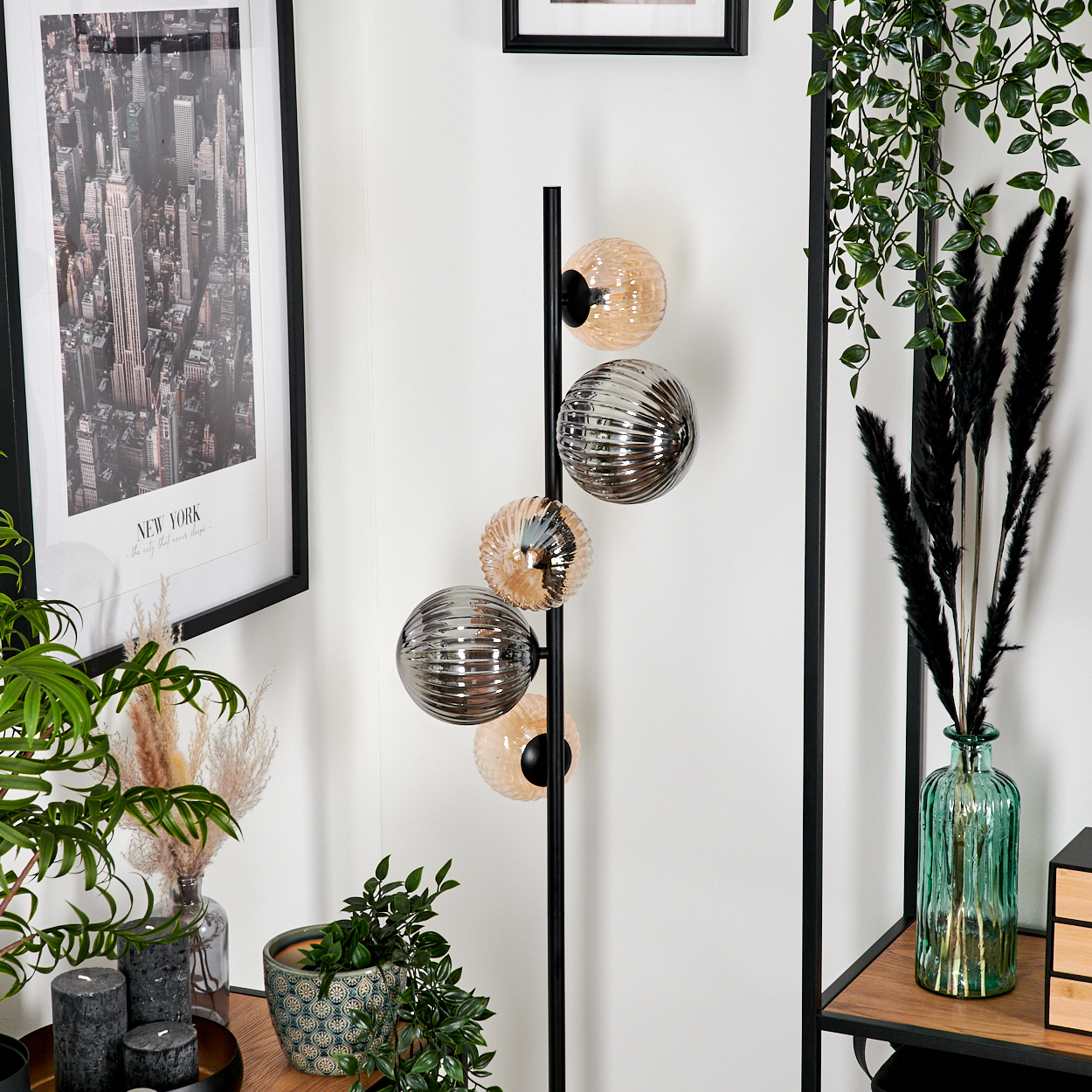Ein modernes Wohnzimmer mit einer hohen Lampe mit Kugelleuchten, einem gerahmten New York-Druck und verschiedenen Pflanzen und Dekorationen.