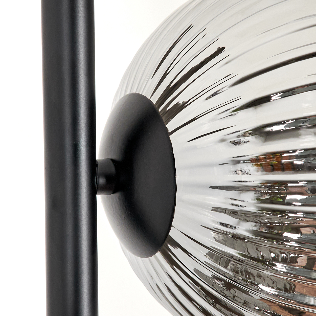 Nahaufnahme einer schwarzen Lampe. Eine klare, geriffelte Glaskugel ist an einer schwarzen Stange befestigt. Weißer Hintergrund.