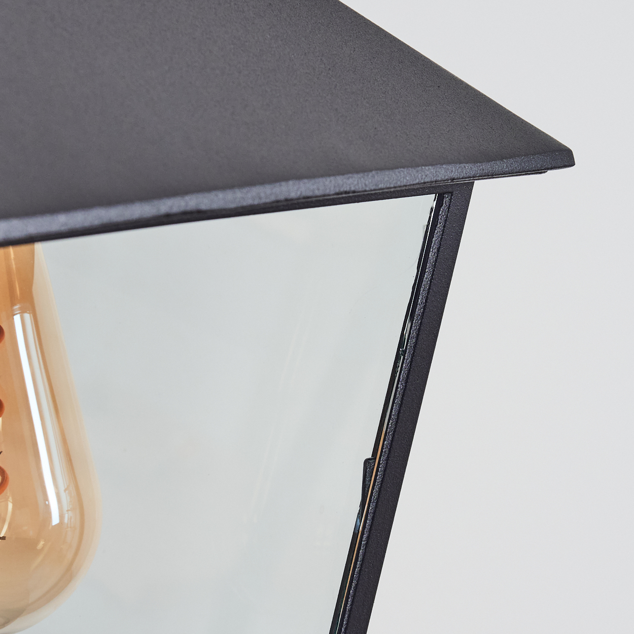 Nahaufnahme einer schwarzen Lampe mit Glasscheibe, die eine Glühbirne enthält. Die Glühbirne ist orange. Der Hintergrund ist weiß.