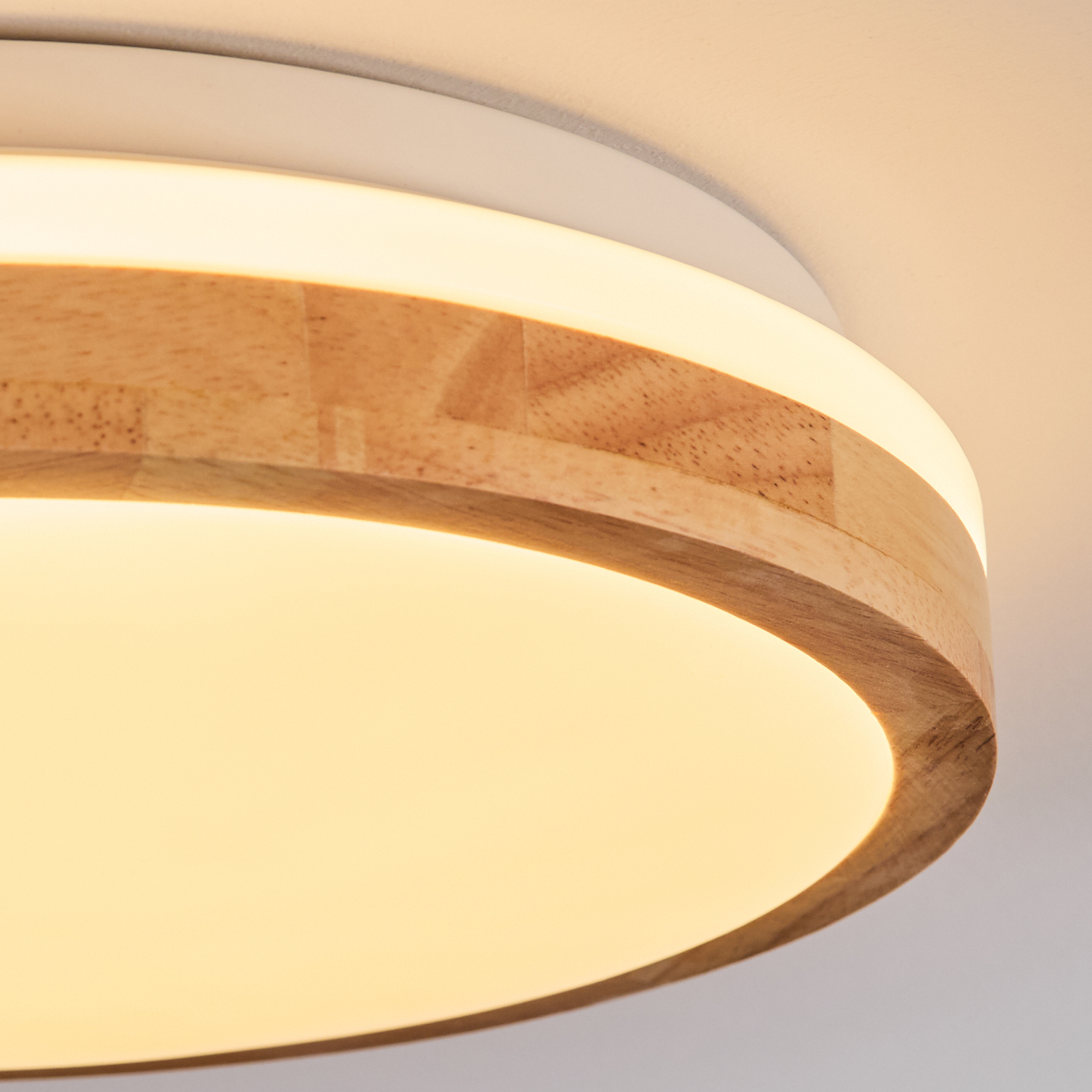 Nahaufnahme einer modernen Deckenleuchte. Sie hat einen Holzring, einen weißen Rahmen und ein helles, warmes Licht. Der Hintergrund ist eine weiße Decke.