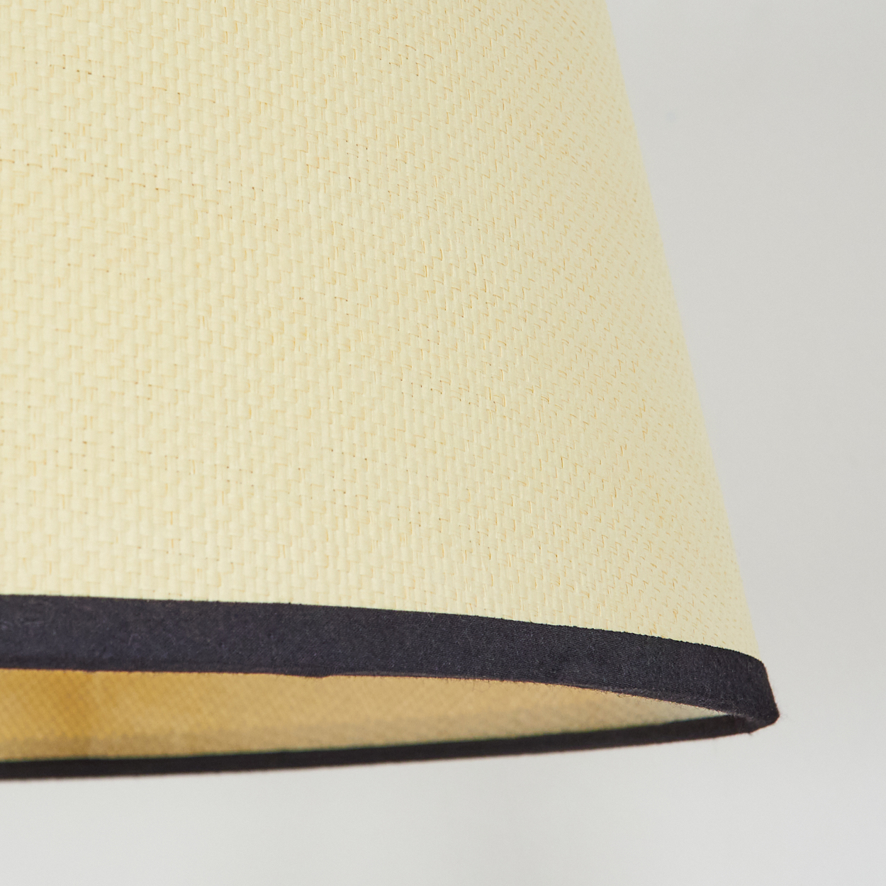 Nahaufnahme eines Lampenschirms. Er hat eine beige gewebte Textur, ein dunkles Band am Boden und einen weißen Hintergrund.