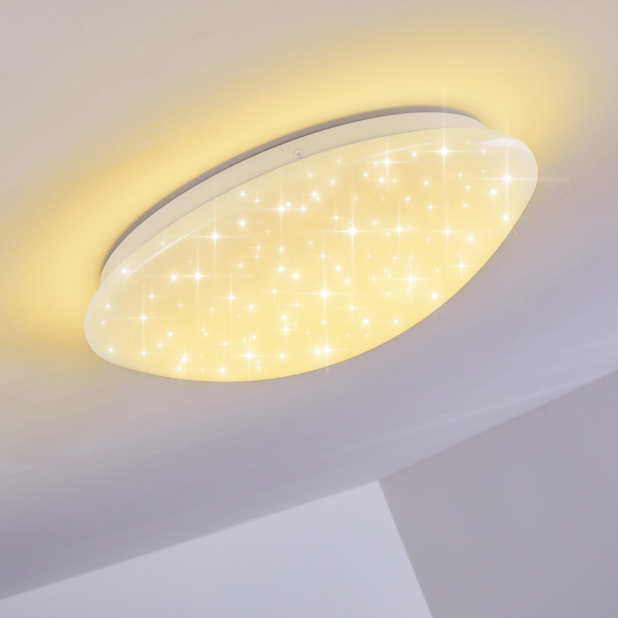 Eine Deckenleuchte mit weißem, ovalem Rahmen und sternförmigem Lichtmuster, an einer weißen Decke befestigt.