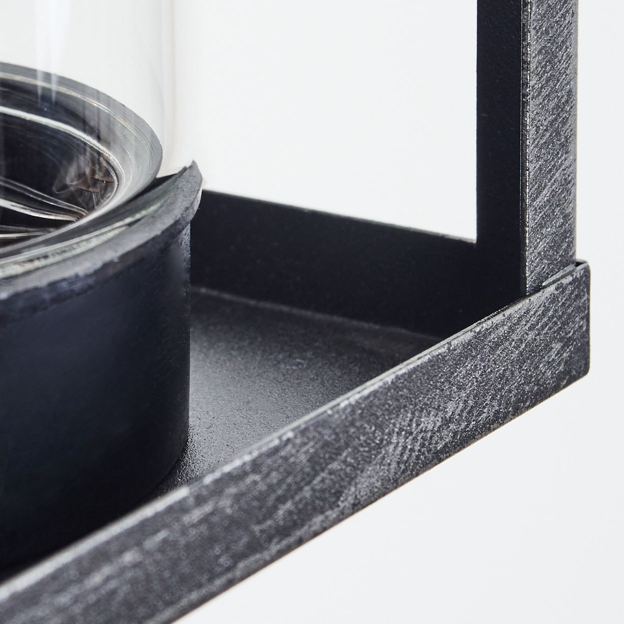 Nahaufnahme eines schwarzen Metallregals mit einem Glasobjekt darauf, weißer Hintergrund.