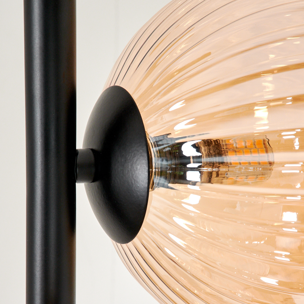 Nahaufnahme einer Lampe. Sie hat einen schwarzen Pfosten und einen runden, gerippten, bernsteinfarbenen Glasschirm. Im Schirm ist eine Glühbirne zu sehen.