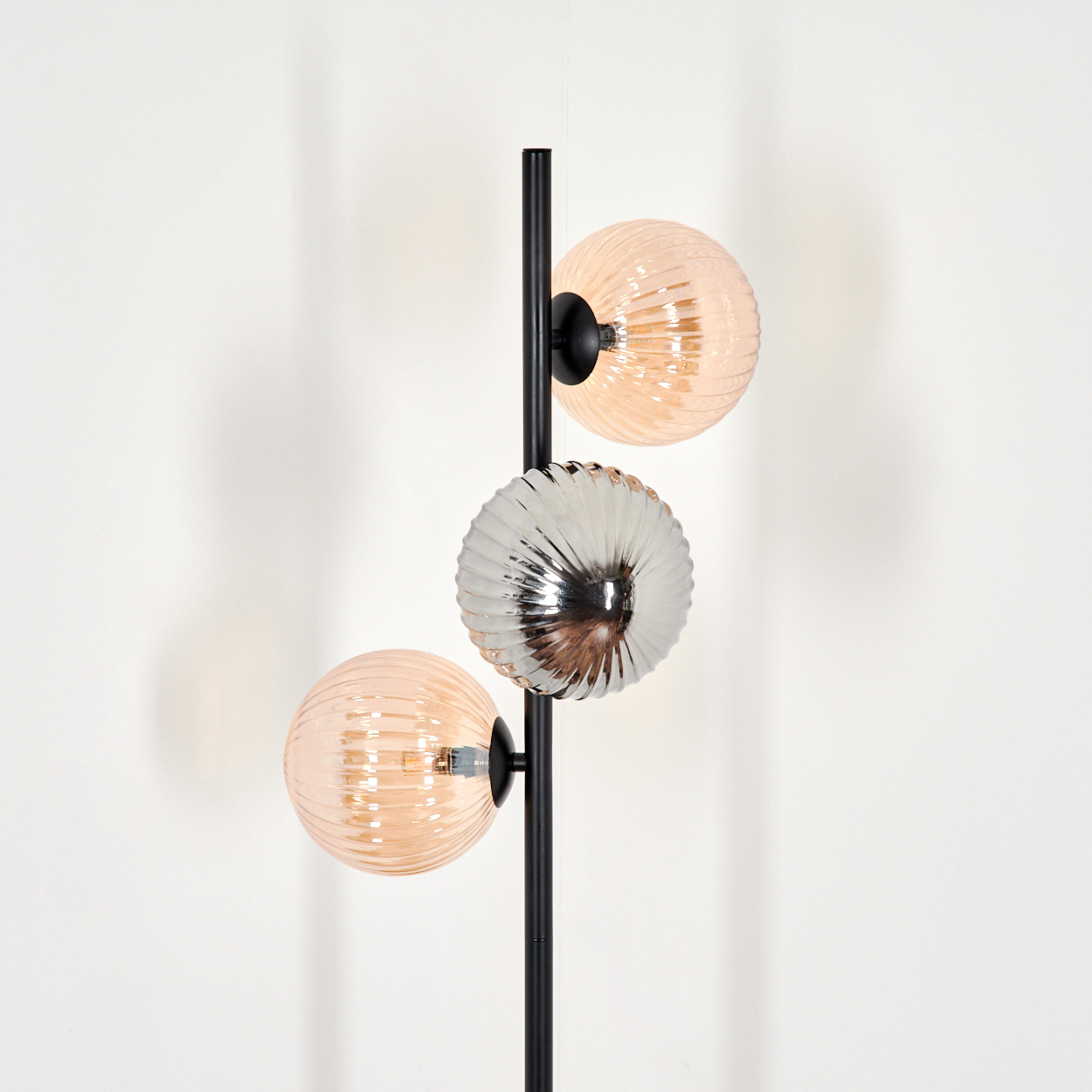 Moderne Lampe mit drei kugelförmigen Schirmen. Zwei sind pfirsichfarben, einer silbern. Schwarzer Pfahl auf weißem Hintergrund.