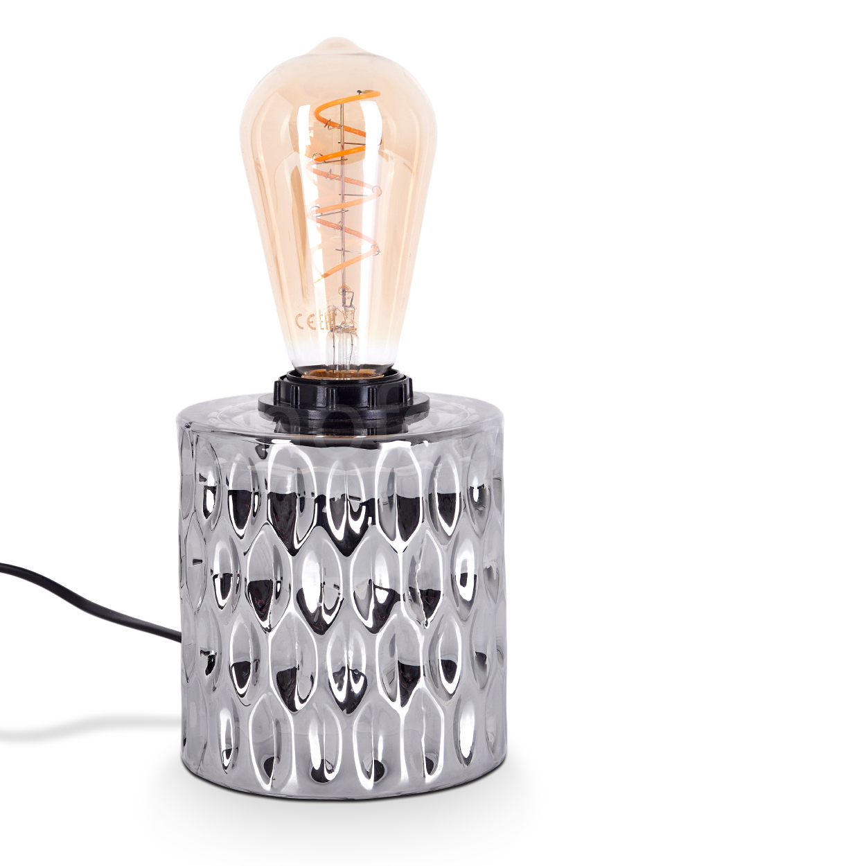 Eine silberne, strukturierte Tischlampe mit einer großen, bernsteinfarbenen Glühbirne. Ein schwarzes Kabel geht von der Lampe ab. Weißer Hintergrund.