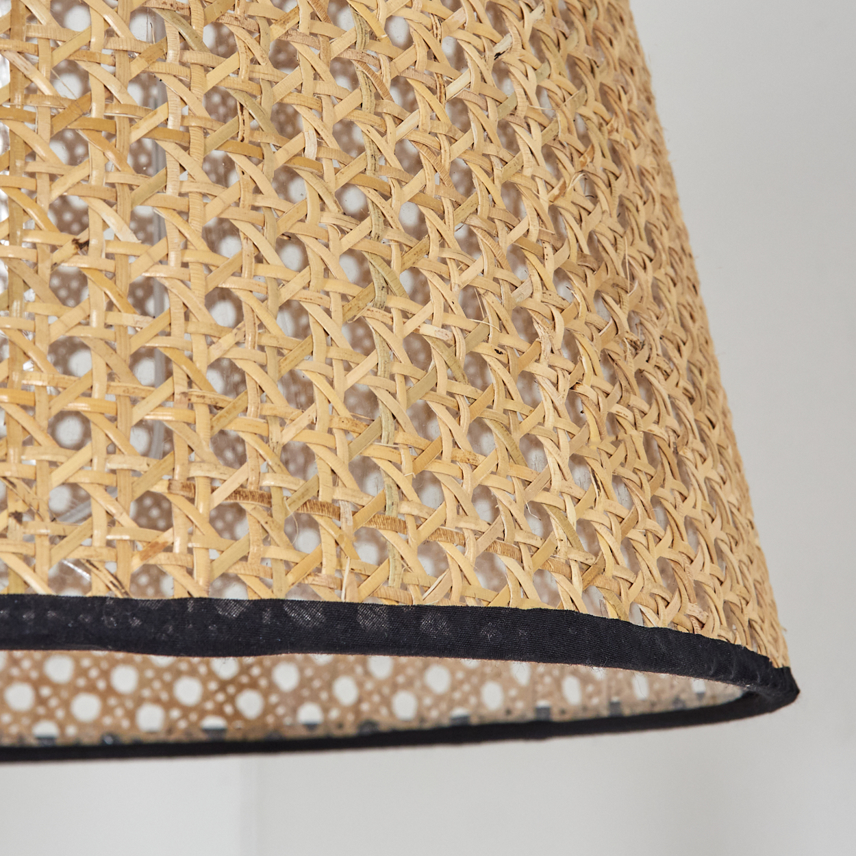 Nahaufnahme eines Lampenschirms mit geflochtenem Rattandesign und schwarzem Rand. Der Hintergrund ist eine weiße Wand.