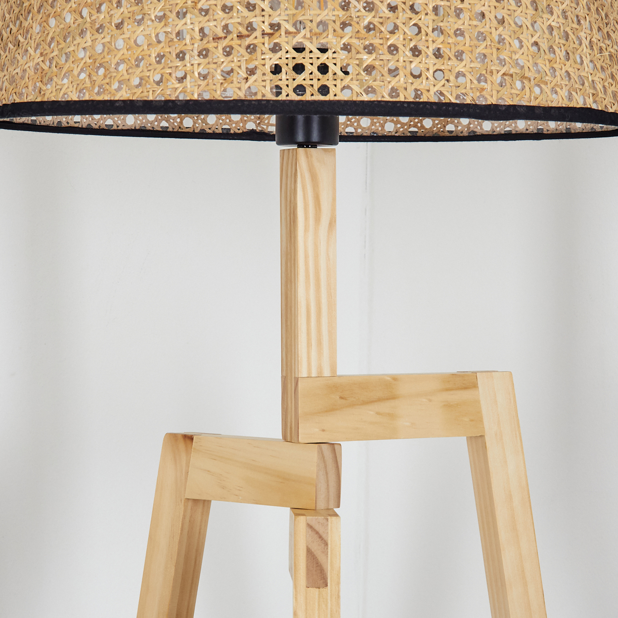 Eine Stehlampe aus Holz mit gewebtem Lampenschirm. Der Lampenschirm hat eine schwarze Einfassung und ist hellbraun. Die Beine sind helles Holz.