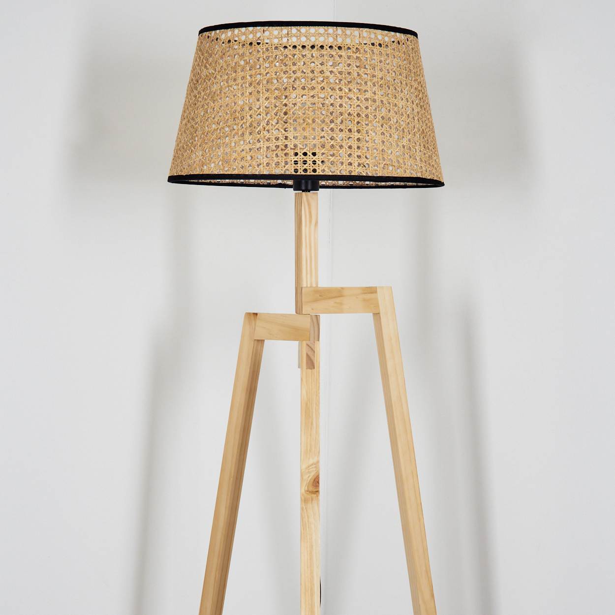 Eine Stehlampe aus Holz mit gewebtem Lampenschirm. Der Lampenschirm ist hellbraun mit schwarzem Rand. Das Gestell ist ein helles Holzstativ.