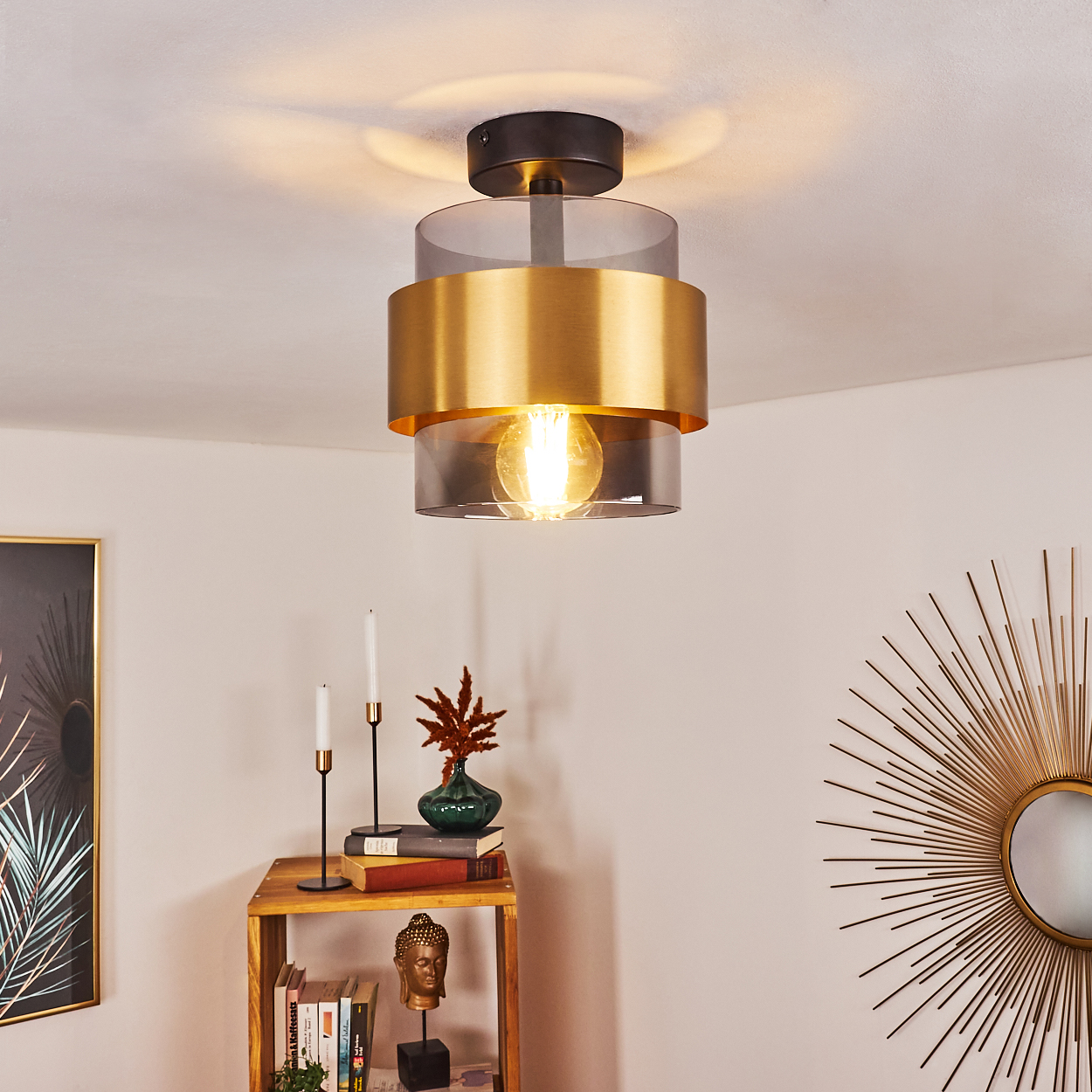 Eine moderne Deckenleuchte mit goldenem Ring, ein Regal mit Dekorationen, ein Wandspiegel, eine Buddha-Statue und eine Vase.