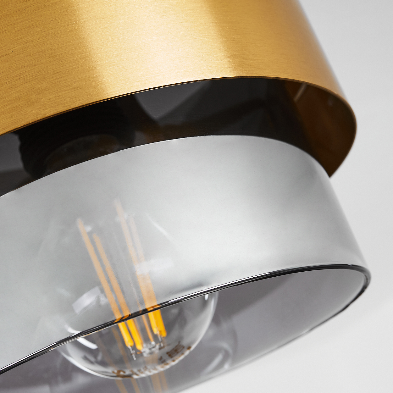 Nahaufnahme einer modernen Lampe. Goldene, schwarze und silberne Schichten umgeben eine klare Glühbirne. Licht scheint, die Elemente beleuchtend.