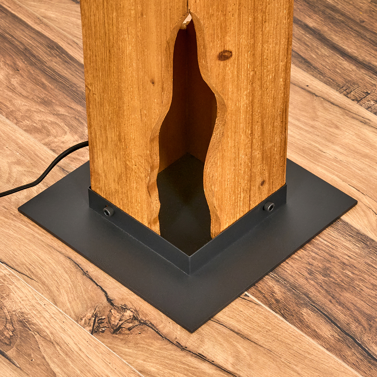 Holzlampenpfosten mit schwarzem Sockel. Das Holz hat einen ausgeschnittenen Abschnitt. Die Lampe steht auf einem Holzboden.