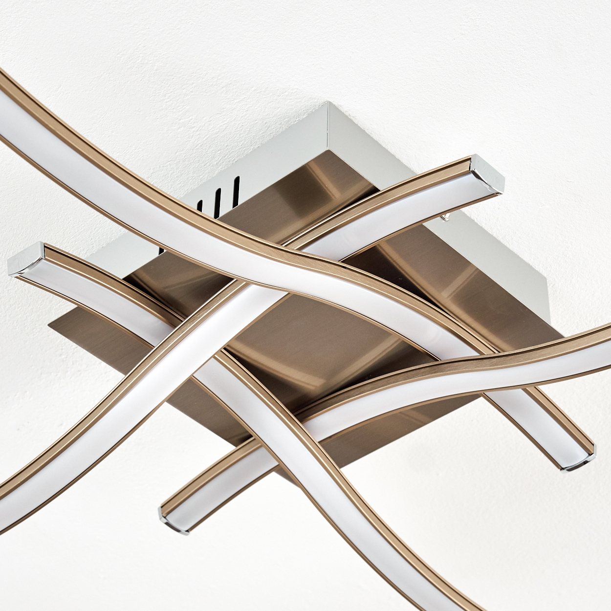 Eine moderne Deckenleuchte. Sie hat gebogene, weiße Lichtstreifen mit goldfarbenen Kanten und eine quadratische Metallbasis.