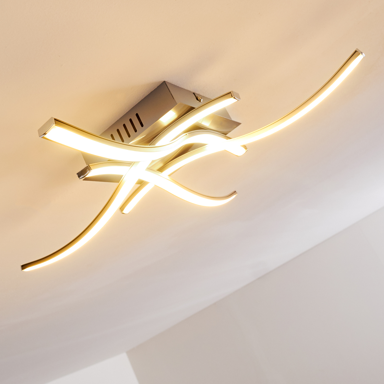 Eine moderne Deckenleuchte mit geschwungenen, leuchtenden Lichtleisten in einem Raum mit weißer Decke.
