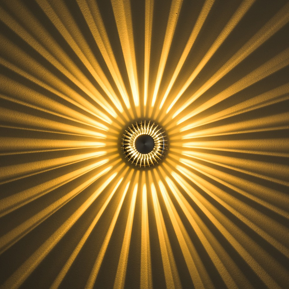 Eine kreisförmige Leuchte an einer Wand, die radiale Schatten wirft. Die Lichtquelle ist hell, umgeben von einem dunklen Ring.