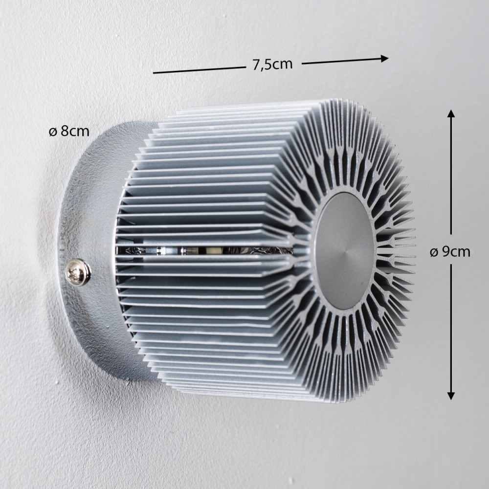 Eine silberne, zylindrische LED-Leuchte ist an einer weißen Wand montiert. Abmessungen sind angegeben: 7,5 cm, 8 cm Durchmesser und 9 cm Höhe.