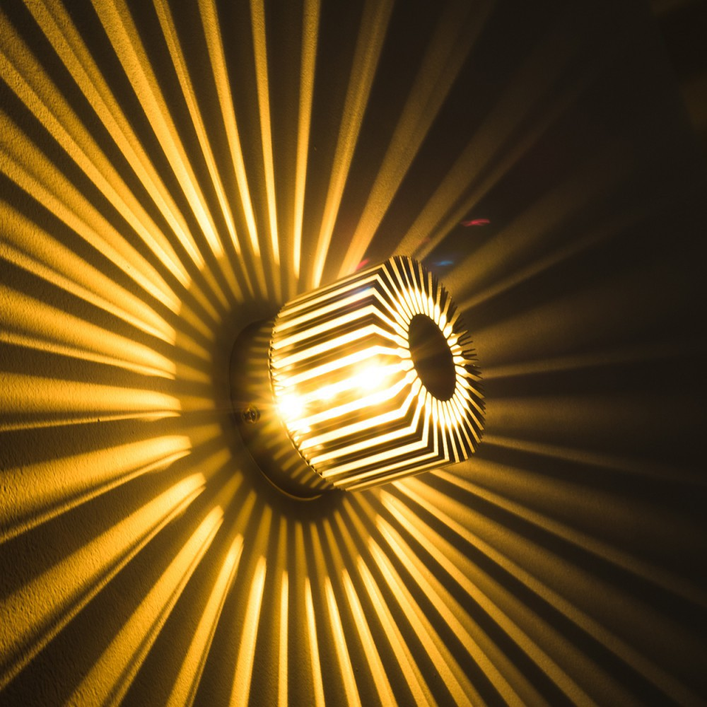 Eine Wandlampe mit geometrischem Design wirft strahlendes Licht und Schatten auf die Wand. Die Lampe ist rund mit einem zentralen Loch.