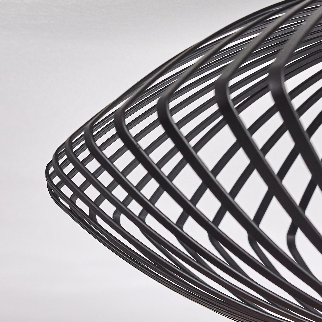 Nahaufnahme eines schwarzen Lampenschirms mit Drahtrahmen vor weißem Hintergrund. Der Schirm hat ein Spiraldesign mit gebogenen Metallstäben.