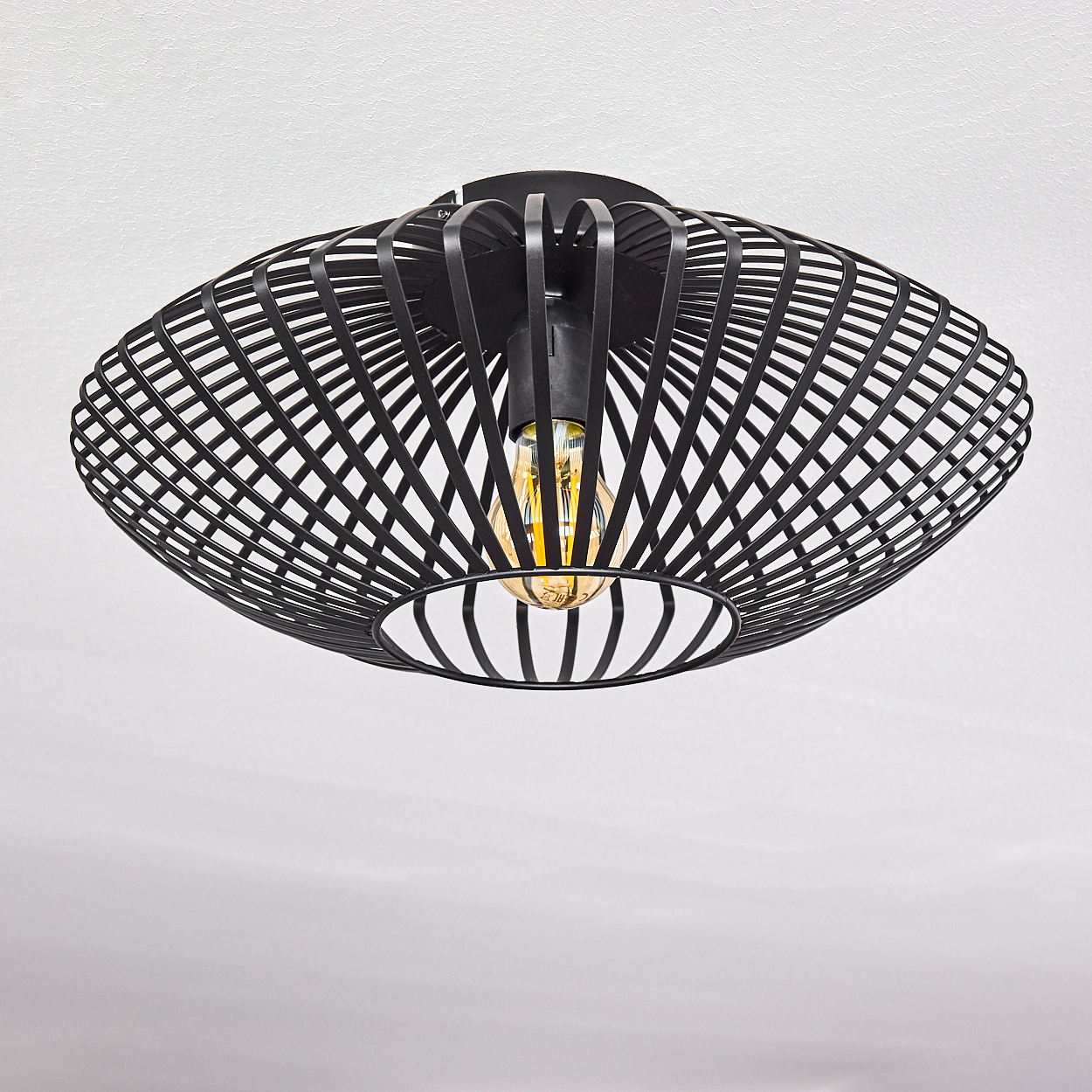 Eine schwarze, moderne Deckenlampe. Sie hat einen käfigartigen Schirm, und eine leuchtende, gelbe Glühbirne ist sichtbar. Der Hintergrund ist weiß.