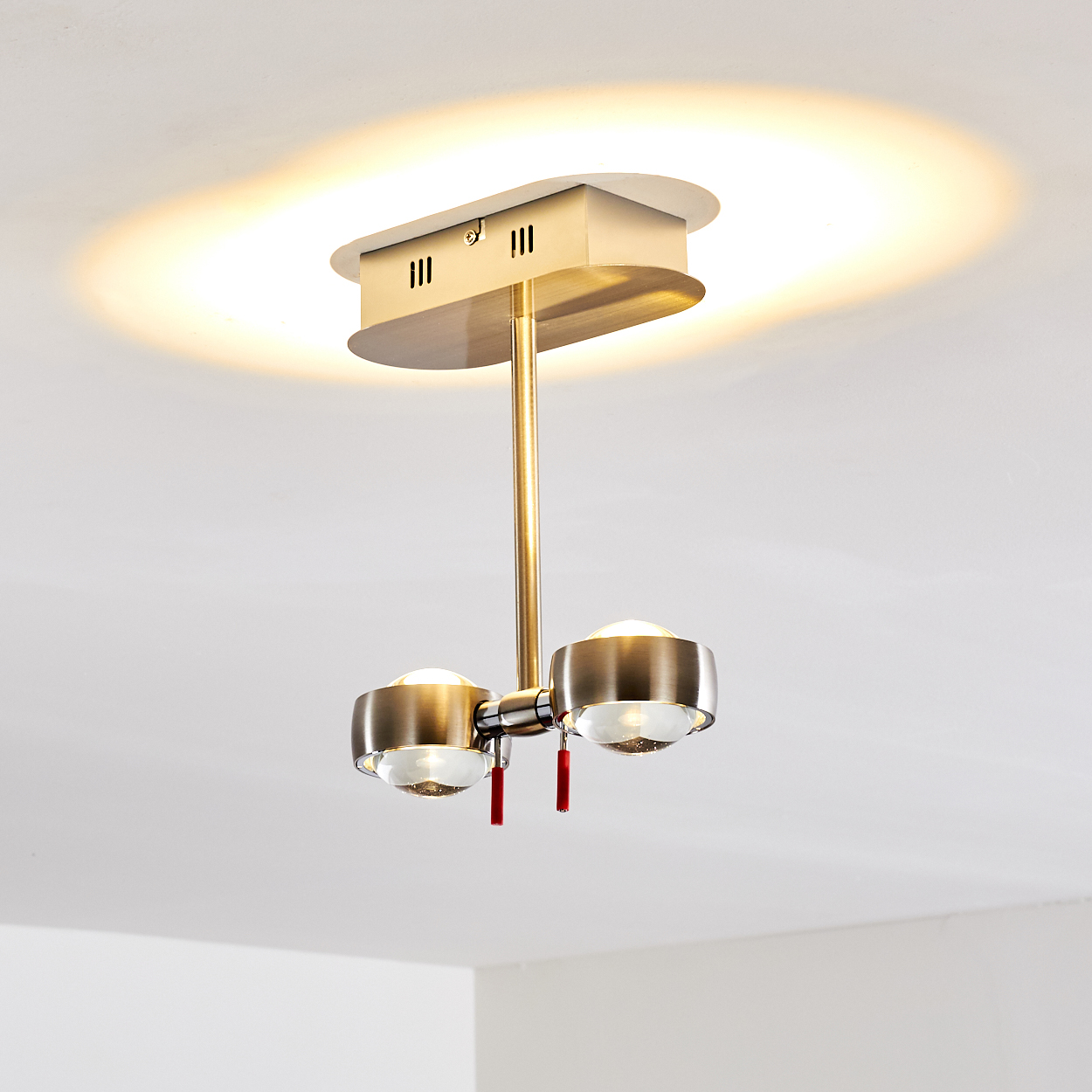 Moderne Deckenleuchte mit zwei Lichtern, Messingausführung und roten Quasten. Die Decke ist weiß.