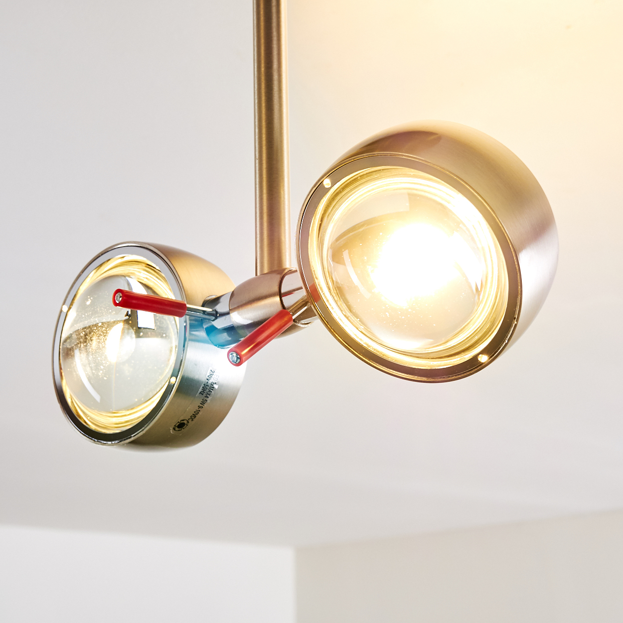 Zwei metallische Scheinwerfer mit Glasabdeckungen. Die Lichter sind an und werfen einen warmen Schein. Rote Griffe sind sichtbar. Weißer Hintergrund.