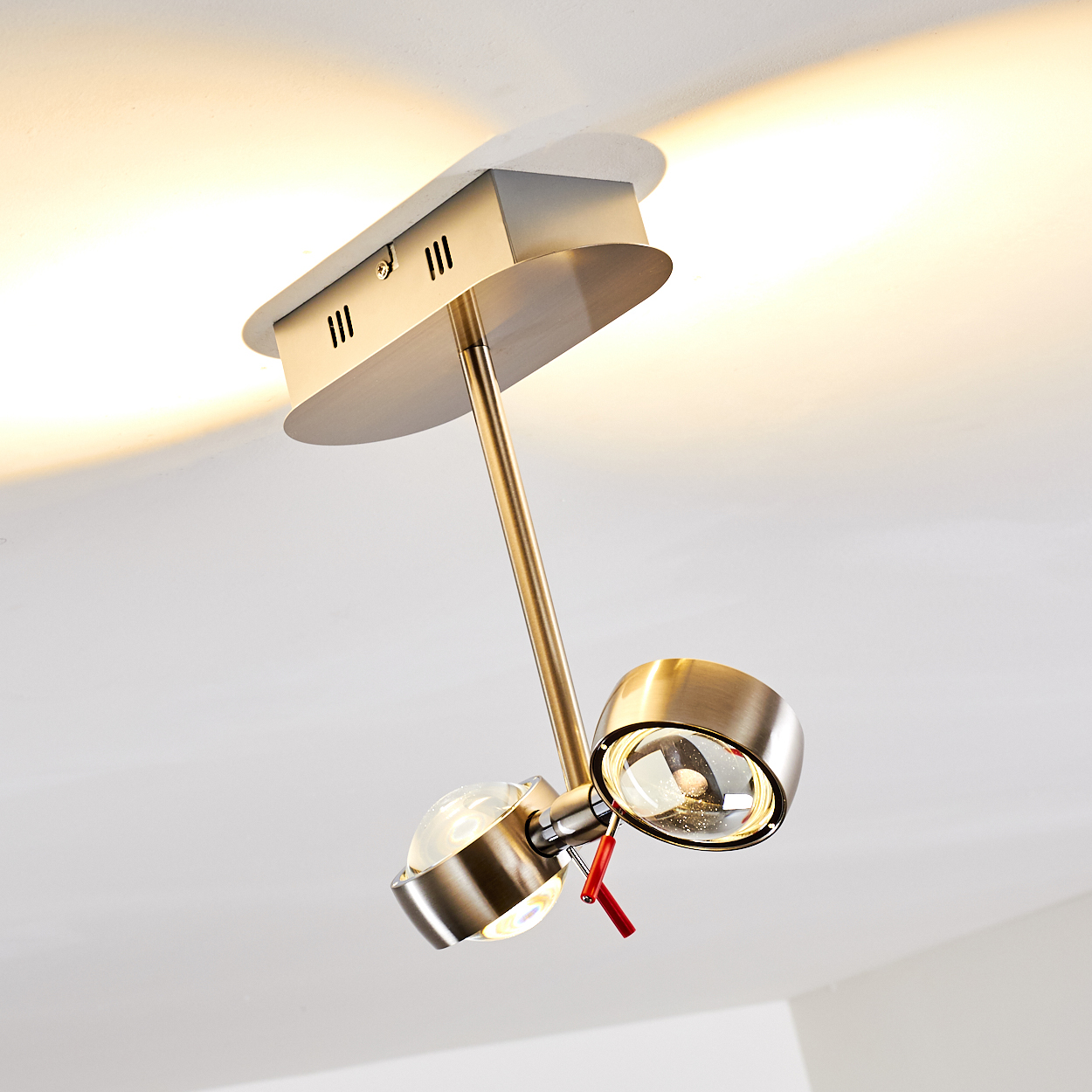 Moderne Deckenleuchte mit zwei Strahlern. Metallausführung, roter Schalter. Helle Beleuchtung vor weißer Decke.