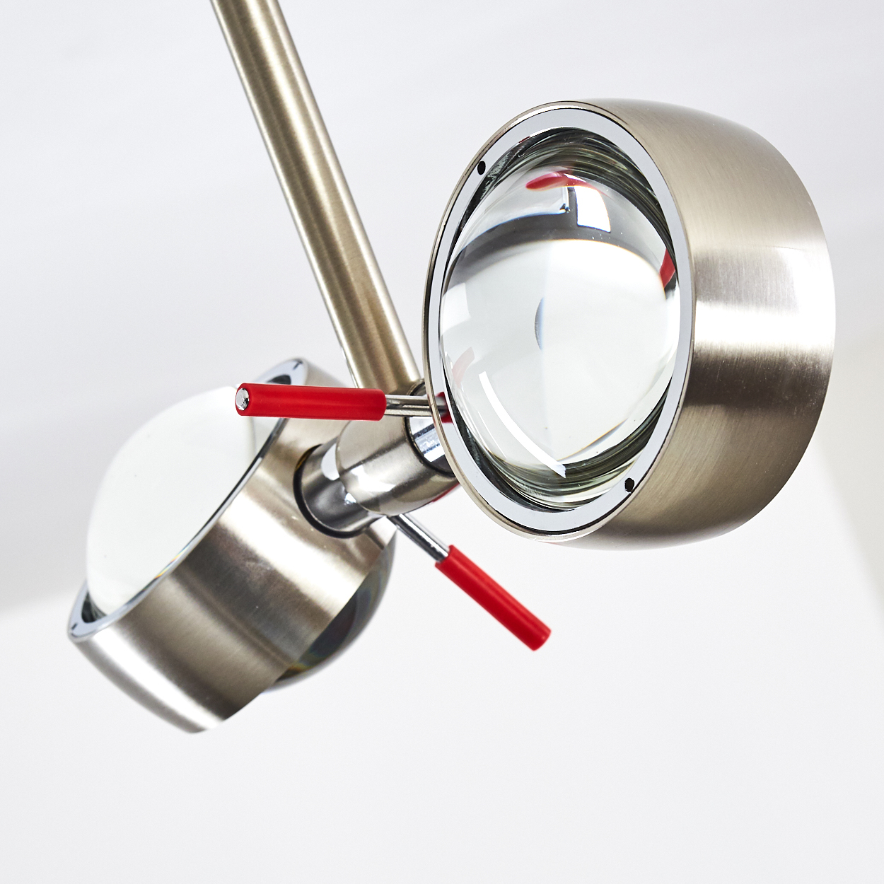 Moderne silberne Lampe mit zwei runden Leuchten, klaren Linsen und roten Griffen auf weißem Hintergrund.