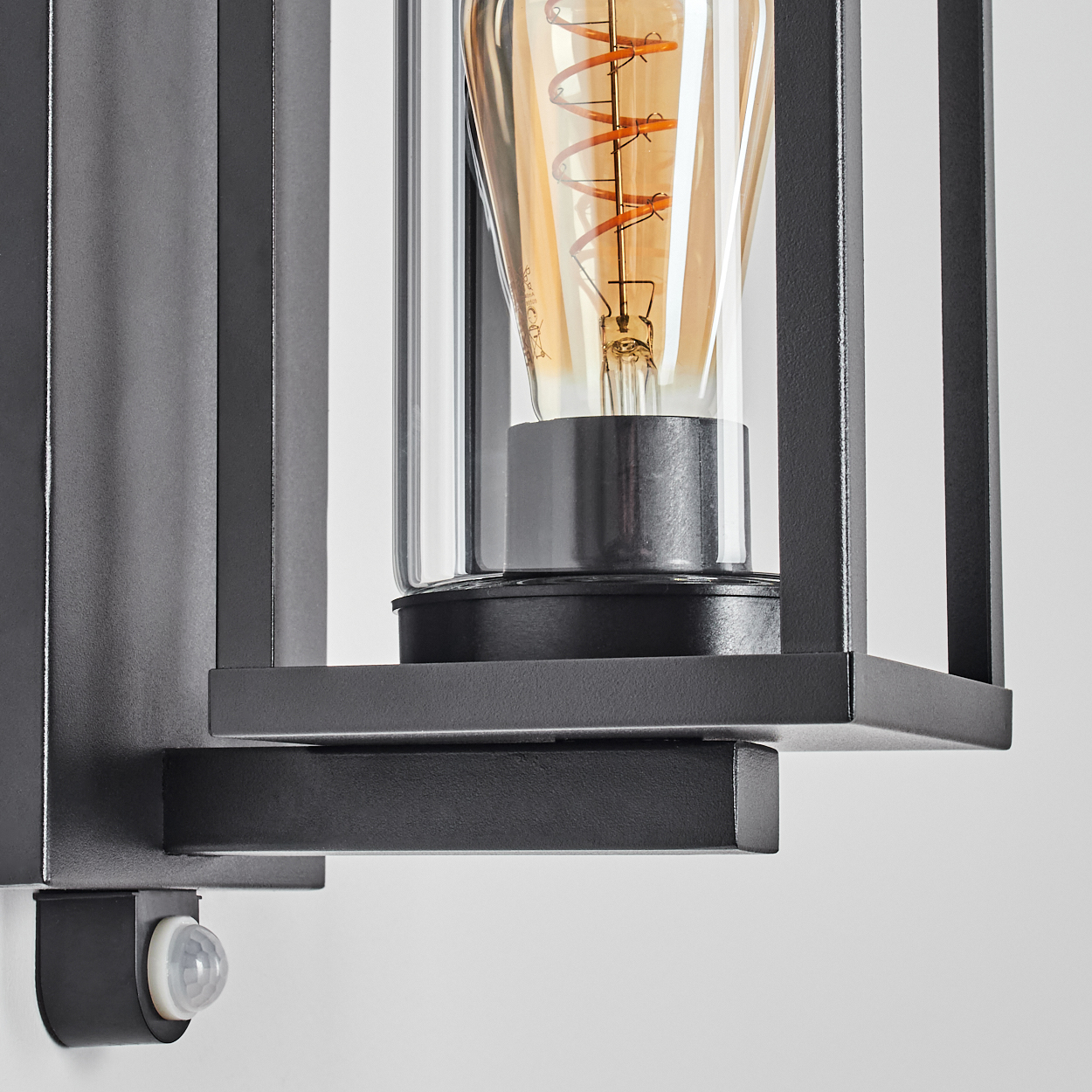 Nahaufnahme einer schwarzen Außenlampe mit einer glaseingeschlossenen Glühbirne. Ein Bewegungsmelder befindet sich unter der Lampe.